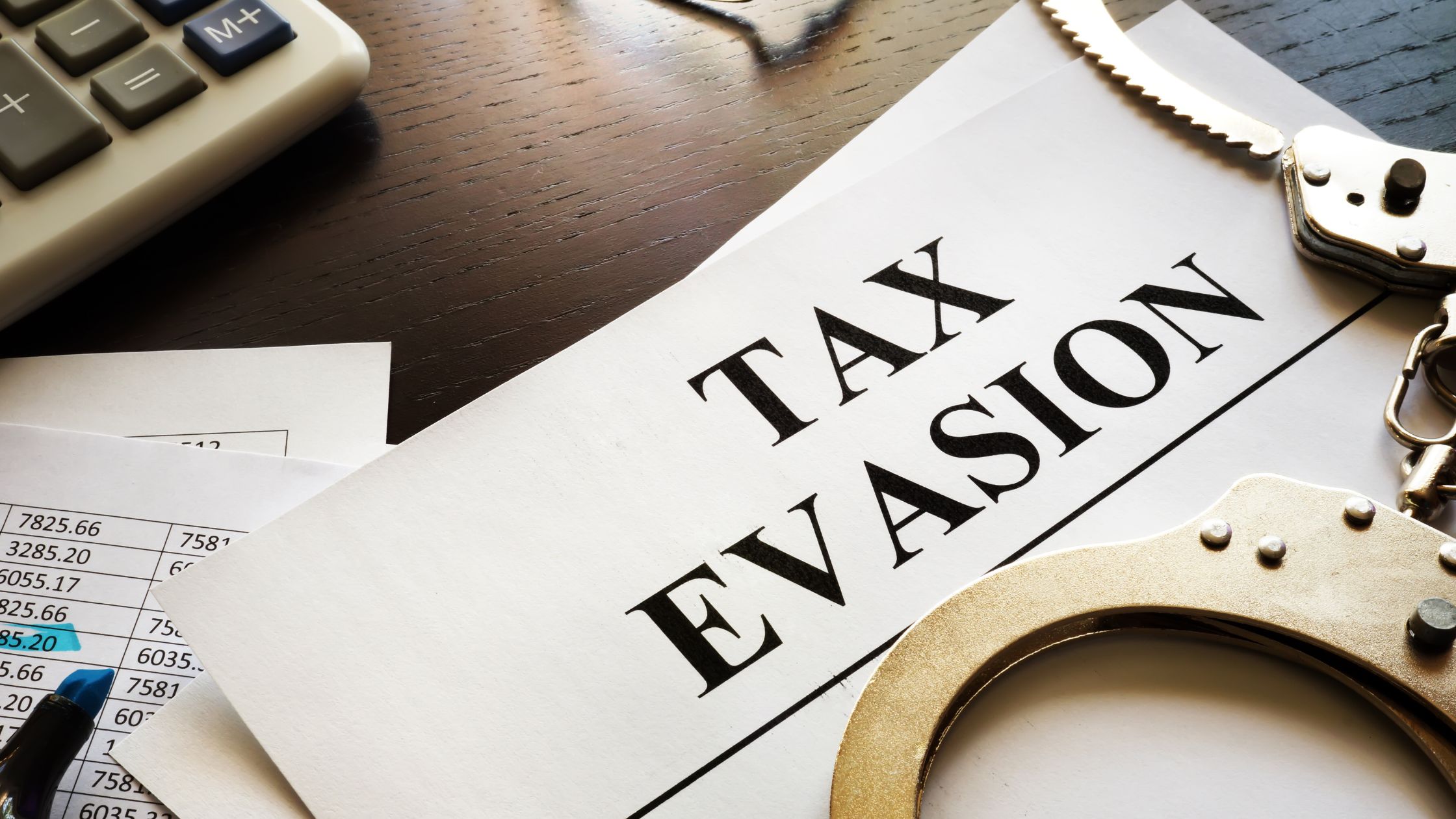 The words Alleviate Tax evasion printed on paper with a calculator in the corner and handcuffs on a desk